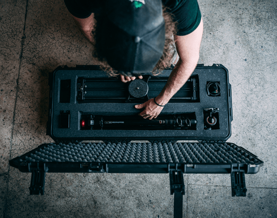 Valise rigide SKB ouverte avec intérieur en mousse stratifiée, dans laquelle l'équipement est soigneusement placé dans des compartiments découpés, vue de dessus pendant qu'une personne ajuste l'intérieur.