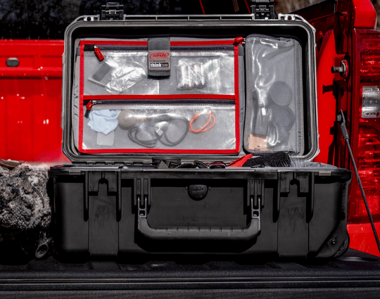 Valise rigide SKB ouverte avec organiseur de couvercle et compartiments transparents à fermeture éclair, remplie de petites pièces et d'accessoires, placée à l'arrière d'un véhicule.
