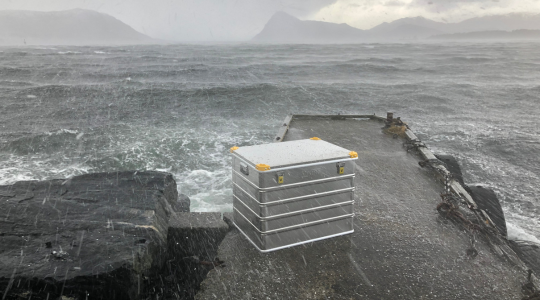 Valise Viking en aluminium étanche placée sur une jetée en bord de mer par forte pluie et conditions météorologiques difficiles.